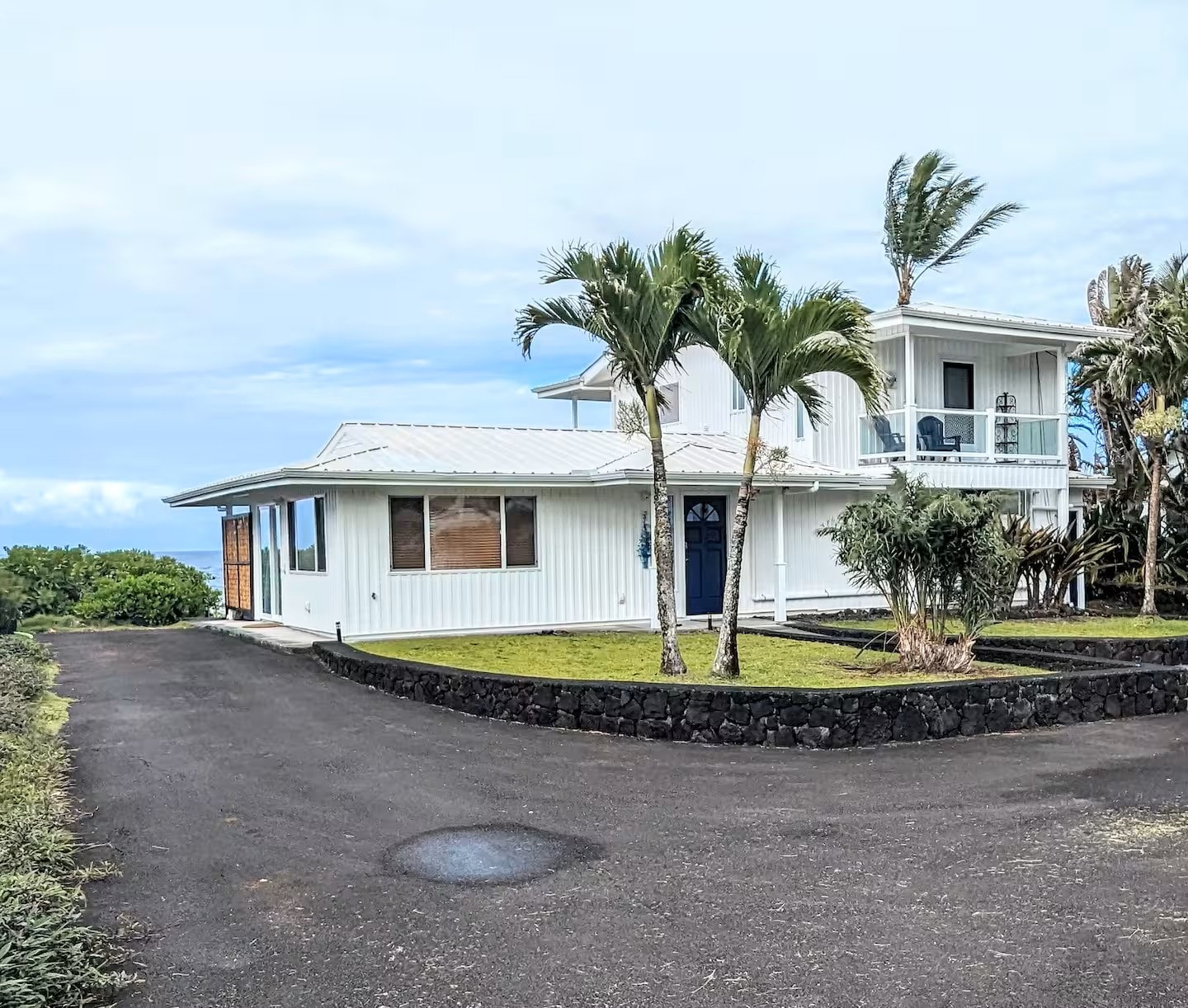 Front of Maka Ala Lani — white house with lava rock wall, palm trees, and ocean in the background
